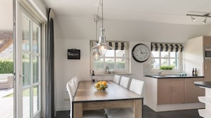 Eine moderne Küche mit einem Holztisch, weißen Stühlen, einer Uhr und einem Fenster mit Vorhängen.