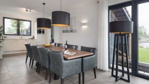Et moderne spiseområde med et træbord, grå polstrede stole og hængende sorte lamper.