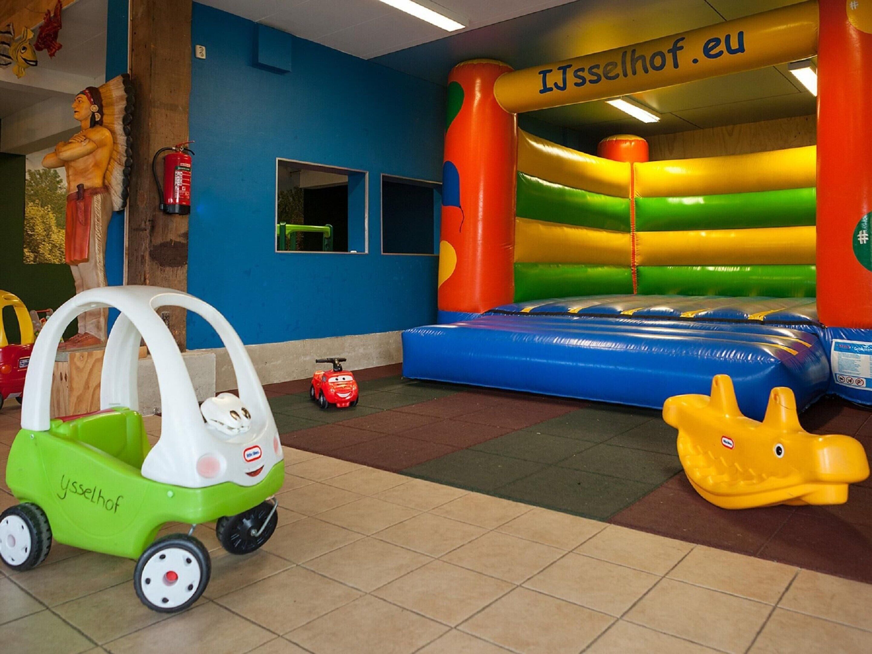 A children's play area with a bouncy castle, a toy car, and a toy dinosaur.