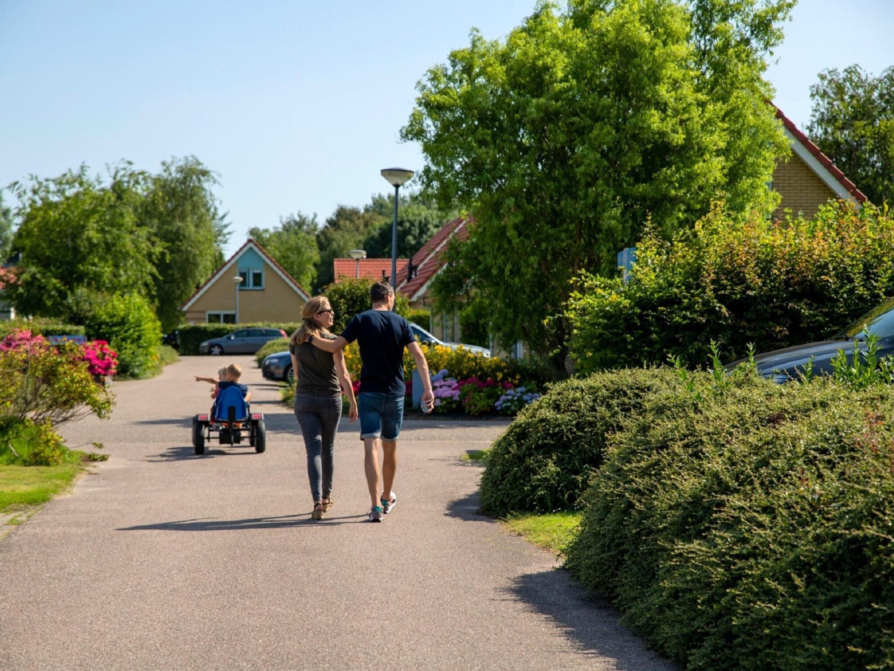 A residential street with houses, a child on a tricycle, and a couple walking.