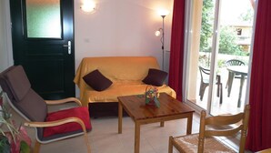 A room with a sofa, two chairs, a small table with a flower vase, a door with frosted glass, and a view through a sliding glass door. - Dordogne Escape w/ Shared Pools (Gavaudun)