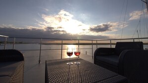 Blick auf einen Sonnenuntergang von einem Balkon, auf dem sich zwei Gläser Rotwein befinden.
