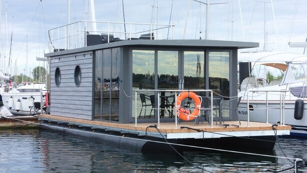 Ein modernes Boot mit einer verglasten Kabine, einem kleinen Deck mit Sitzgelegenheiten und einem Rettungsring.