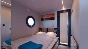 Ein Schlafzimmer mit einem Bett, einem Rundfenster, einer Tür mit Jalousien und einem an der Wand hängenden Bild.