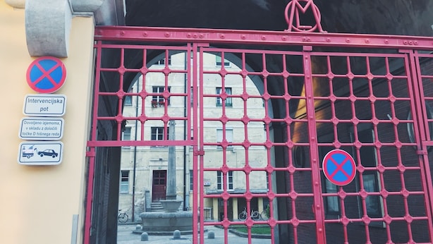 A red gate with a grid pattern, a statue on the left, and a building in the background.