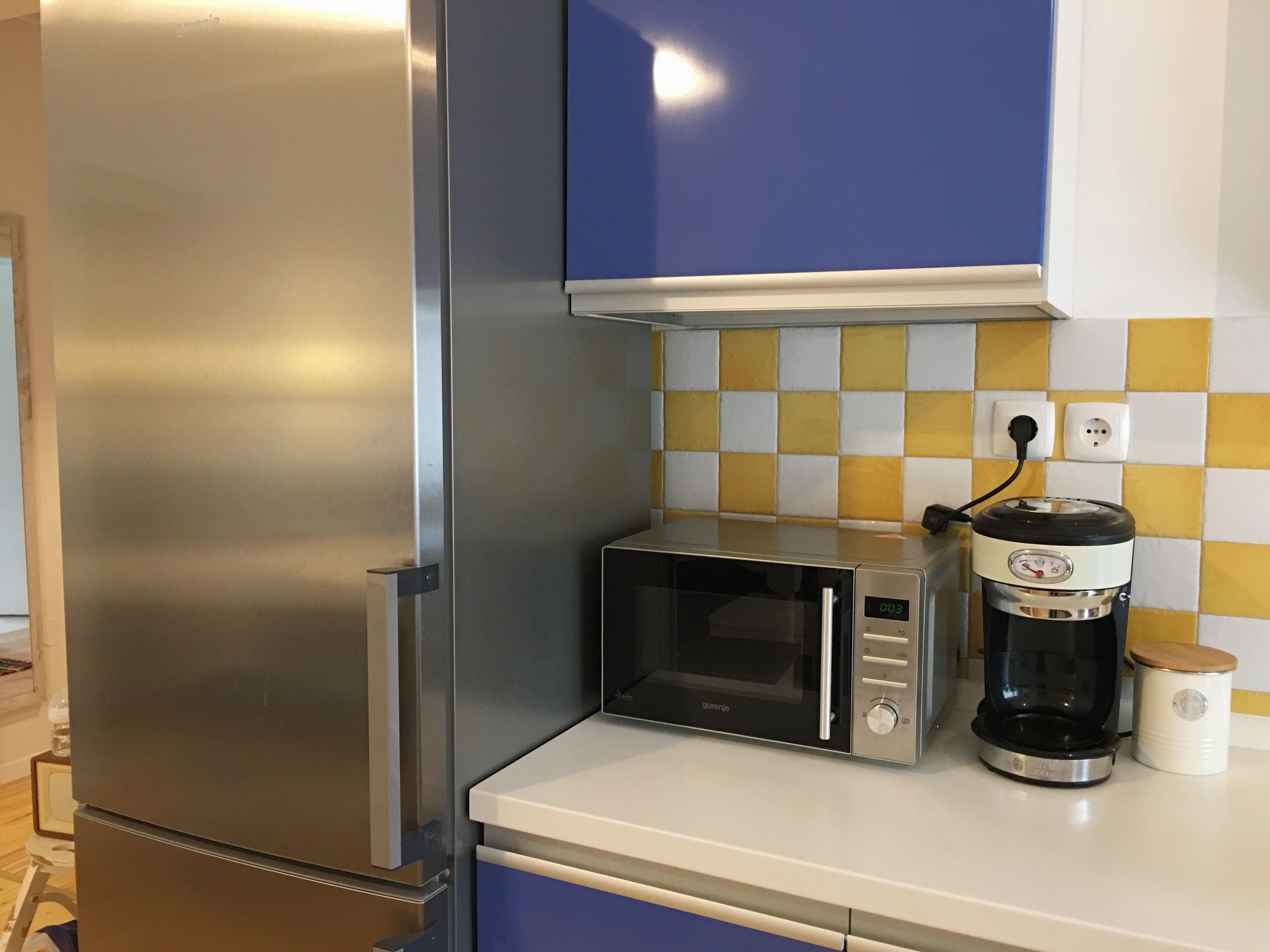 Una cocina con un refrigerador de acero inoxidable, un microondas y una cafetera en la encimera.