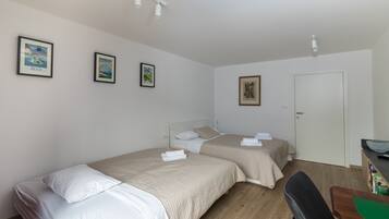 A room with two beds, a desk, and a door. There are framed pictures on the wall.