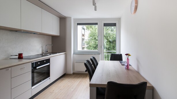 A modern kitchen with white cabinets, a wooden dining table, and a window with a view of greenery. - Jojo Apartment (Ljubljana)