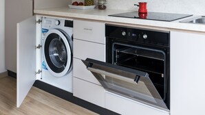 A compact kitchen with built-in appliances, including a washing machine, oven, and a small countertop with a red pot. - Jojo Apartment (Ljubljana)