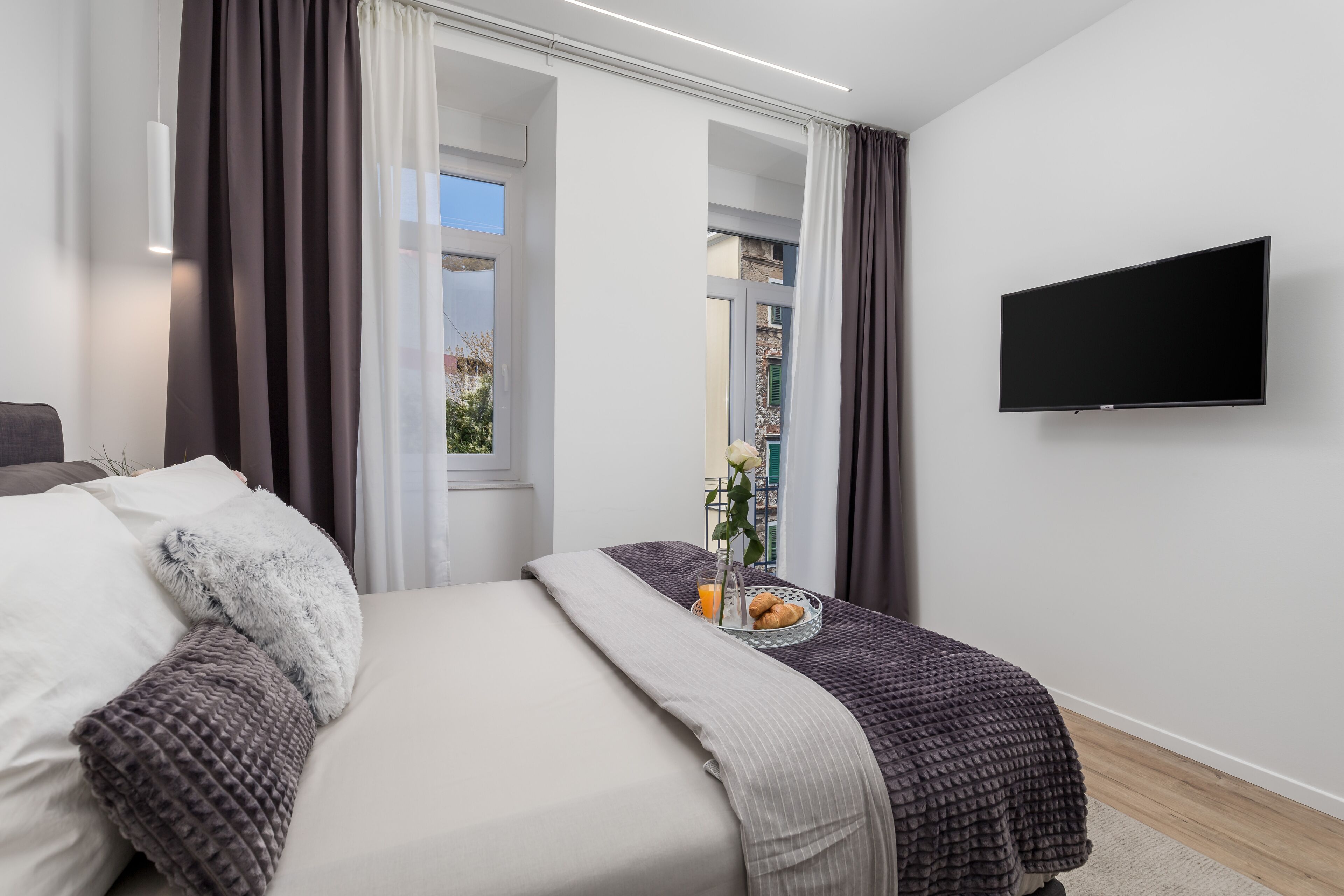 Un dormitorio moderno con cama, cortinas, un televisor de pantalla plana y ventana con vistas.
