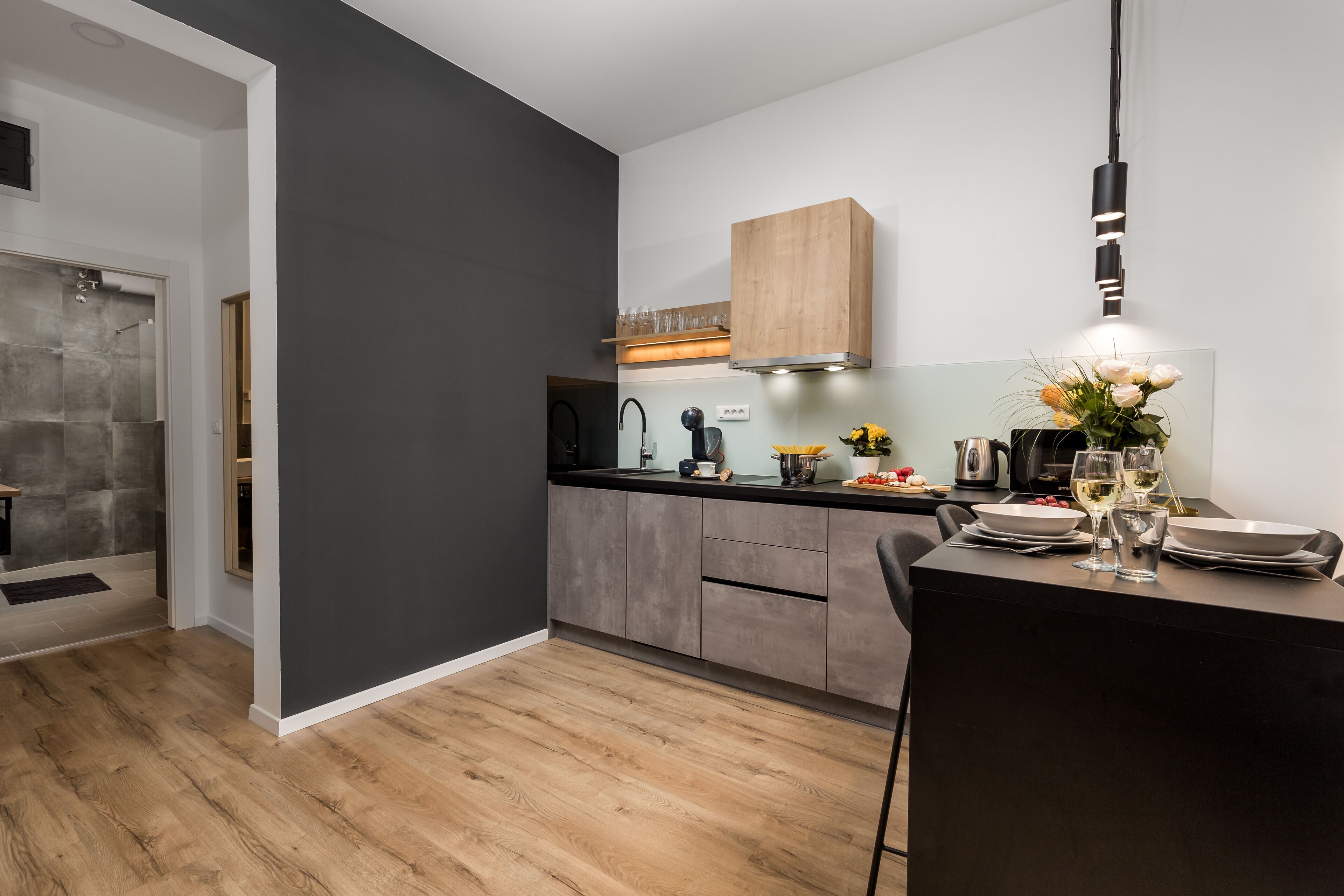 A modern kitchen with a dark grey wall, wooden cabinets, and a dining area with a table set for two.