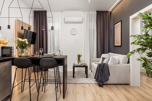 Una sala de estar moderna con un sofá, una mesa de comedor con sillas, una mesita auxiliar con un florero y un ventanal grande con cortinas.