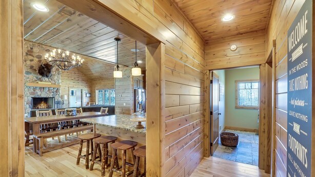 A wooden interior with a stone fireplace, a bar area with stools, and a 'WELCOME' sign. - Wee-Kin-Da-Wa | Getaway at Boyne Mountain | Skybridge View | Ski-In/Ski-Out (Boyne Falls)