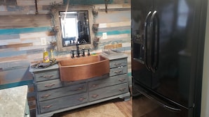 A kitchen with a black refrigerator, a sink with a copper basin, and a mirror with a rustic frame. - Welcome to Riptide Stables, 17 Acre Farm, w/animals by the beach! (Castle Hayne)