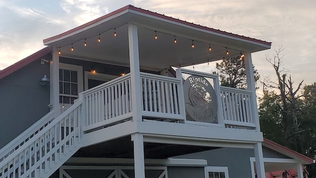 A two-story building with a balcony, string lights, and a sign that reads "Riptide Stable." - Welcome to Riptide Stables, 17 Acre Farm, w/animals by the beach! (Castle Hayne)