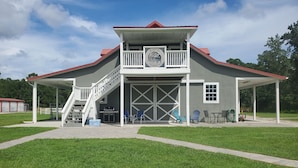 A two-story building with a covered porch, a staircase, and a sign that reads "Riptide Stables". - Welcome to Riptide Stables, 17 Acre Farm, w/animals by the beach! (Castle Hayne)