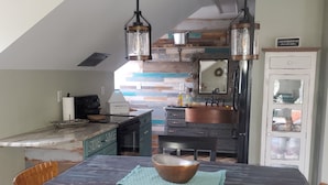 A modern kitchen with a farmhouse aesthetic, featuring a large island, dark cabinetry, and a copper sink. - Welcome to Riptide Stables, 17 Acre Farm, w/animals by the beach! (Castle Hayne)
