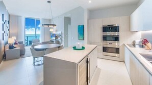 A modern kitchen with a central island, stainless steel appliances, and a dining area with a view. - Hide Ocean Resort (Hollywood)