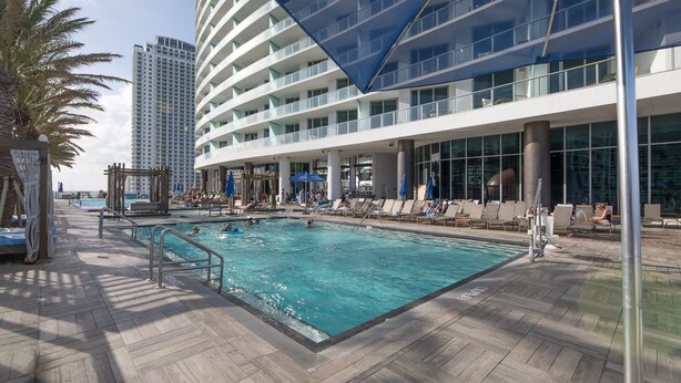A pool area with lounge chairs and umbrellas, surrounded by a modern building with multiple balconies. - Hide Ocean Resort (Hollywood)