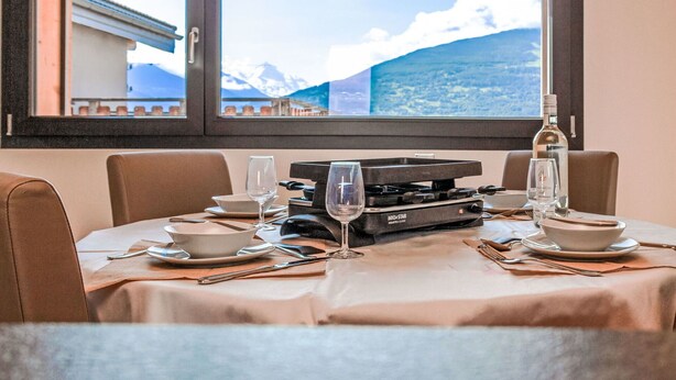 A dining table set with plates, bowls, cutlery, and wine glasses, with a view of mountains through a window. - Stunning private villa for 4 people with WIFI, TV and terrace (Savièse)