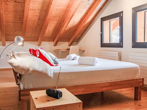 A bedroom with a wooden bed, a bedside lamp, a small table with a radio, and a window with a view of the outside.