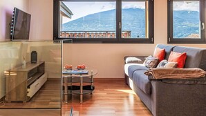 A modern living room with a wooden ceiling, a grey sofa with red cushions, a glass coffee table with oranges, and a TV on a wooden cabinet. - Stunning private villa for 4 people with WIFI, TV and terrace (Savièse)