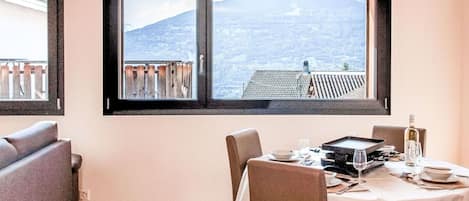 A dining area with a table set for two, a sofa, and a window with a view of a mountainous landscape.