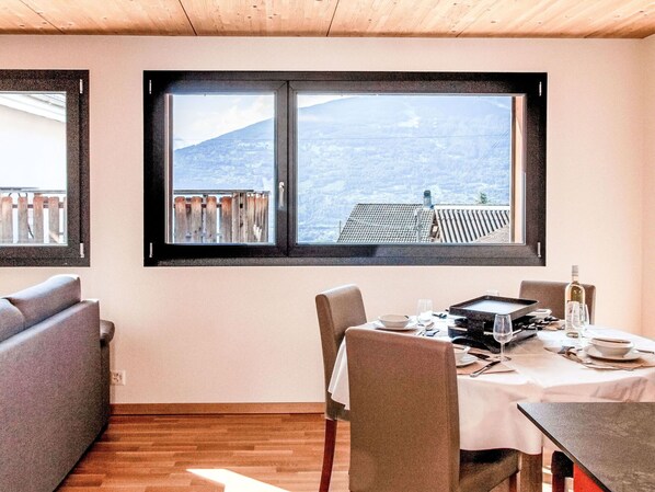 Un coin repas avec une table dressée pour deux personnes, un canapé et une fenêtre donnant sur un paysage montagneux.