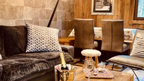 Un salon chaleureux avec un canapé moelleux, une table basse sur laquelle se trouve une bouteille de champagne, des verres à vin et une petite table en bois.