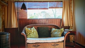Een rieten bank met kussens, een vloerlamp en een radiator in een kamer met houten wanden en een raam.