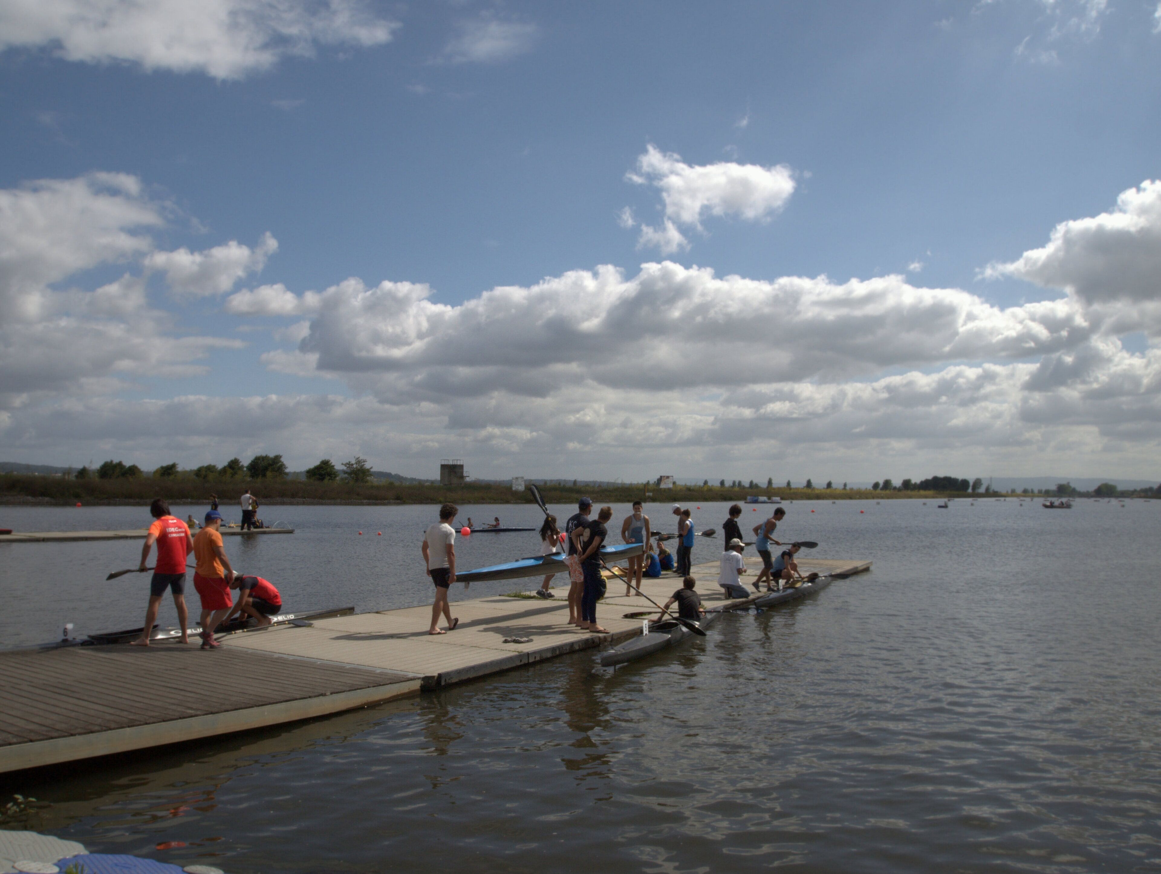 Un muelle con gente preparando canoas para una carrera.