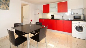 A compact kitchen with red cabinets, a white washing machine, and a dining area with a table and chairs. - Lovely apartment for 4 people with WIFI, pool, A/C, TV and terrace (Benissa)