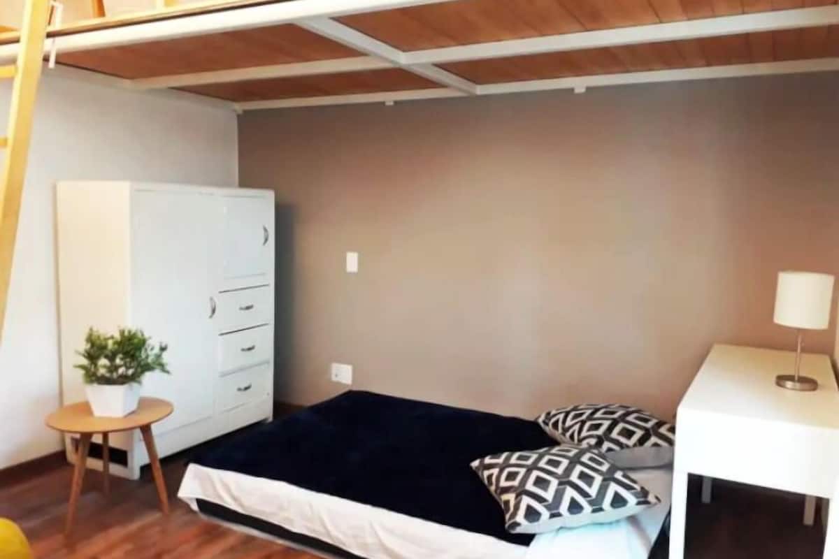 Ein kleiner, kompakter Raum mit einem Etagenbett, einem Schreibtisch inklusive Lampe, einem kleinen Tisch mit Pflanze und einem weißen Kleiderschrank.