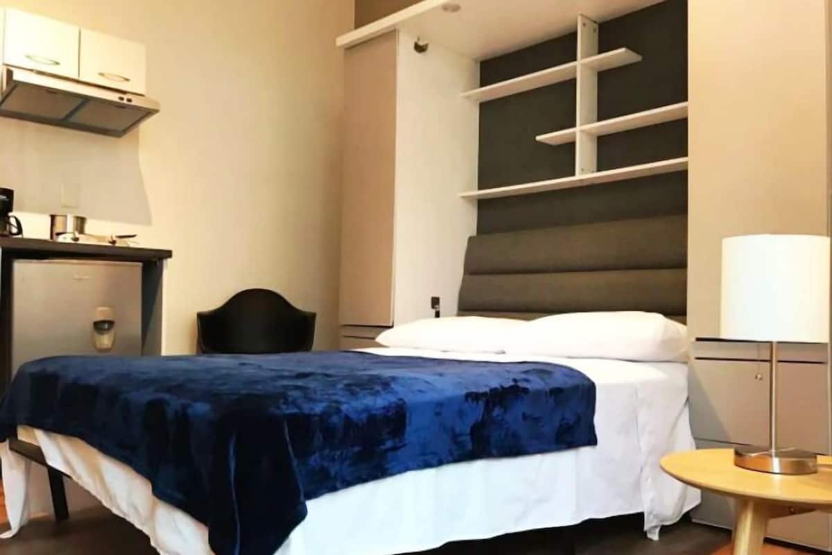 Ein modernes Hotelzimmer mit Bett, Nachttisch, Lampe und Einbauschränken.