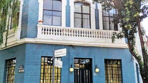 A corner building with a blue facade, a black gate, and a sign indicating a direction.
