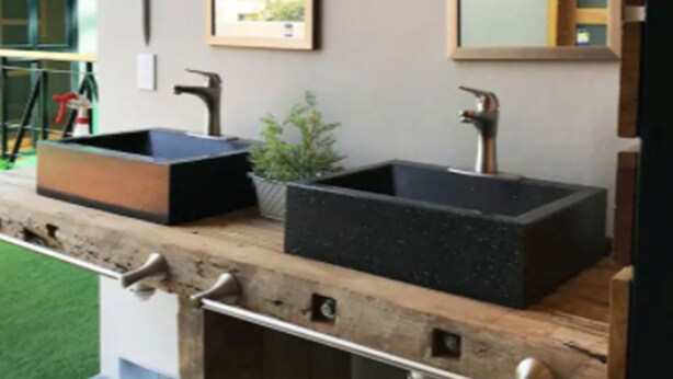 A modern bathroom with two black sinks, a wooden countertop, and a framed picture on the wall.