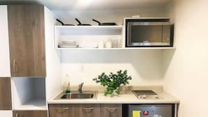 A compact kitchen with a built-in microwave, a sink, and a small refrigerator. - noox Ayuntamiento (Mexico City)
