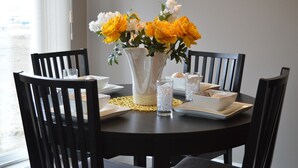 Una mesa de comedor con un jarrón de flores amarillas, platos blancos y vasos de vidrio.