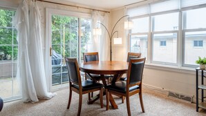 Un coin repas avec une table ronde en bois et quatre chaises, de grandes fenêtres avec des rideaux et un lampadaire.