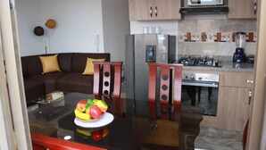En kompakt bolig med et tekøkken, et spisebord med stole, en sofa og en skål med frugt.