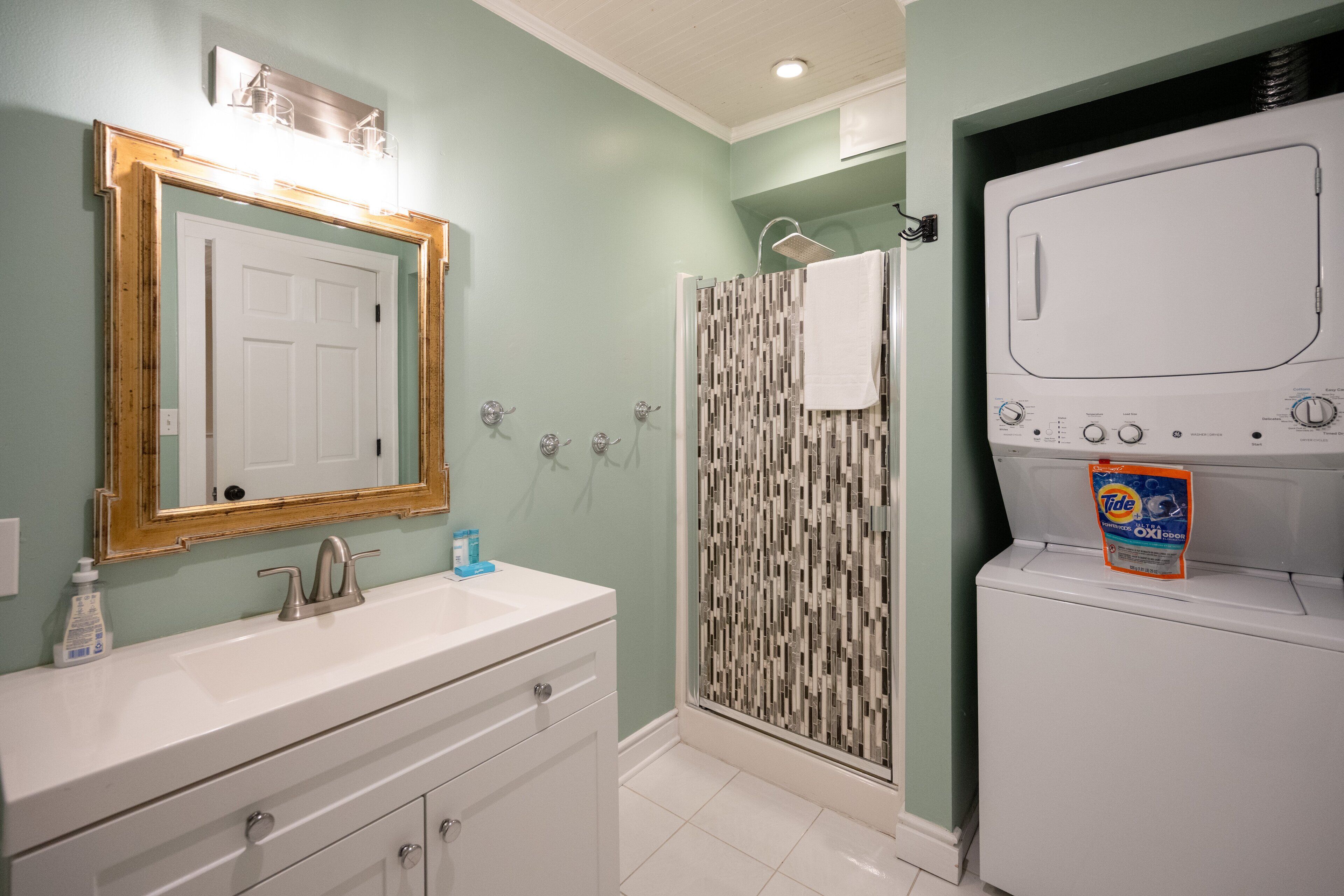 A bathroom with a white sink, a mirror, a shower with a patterned door, and a washing machine.