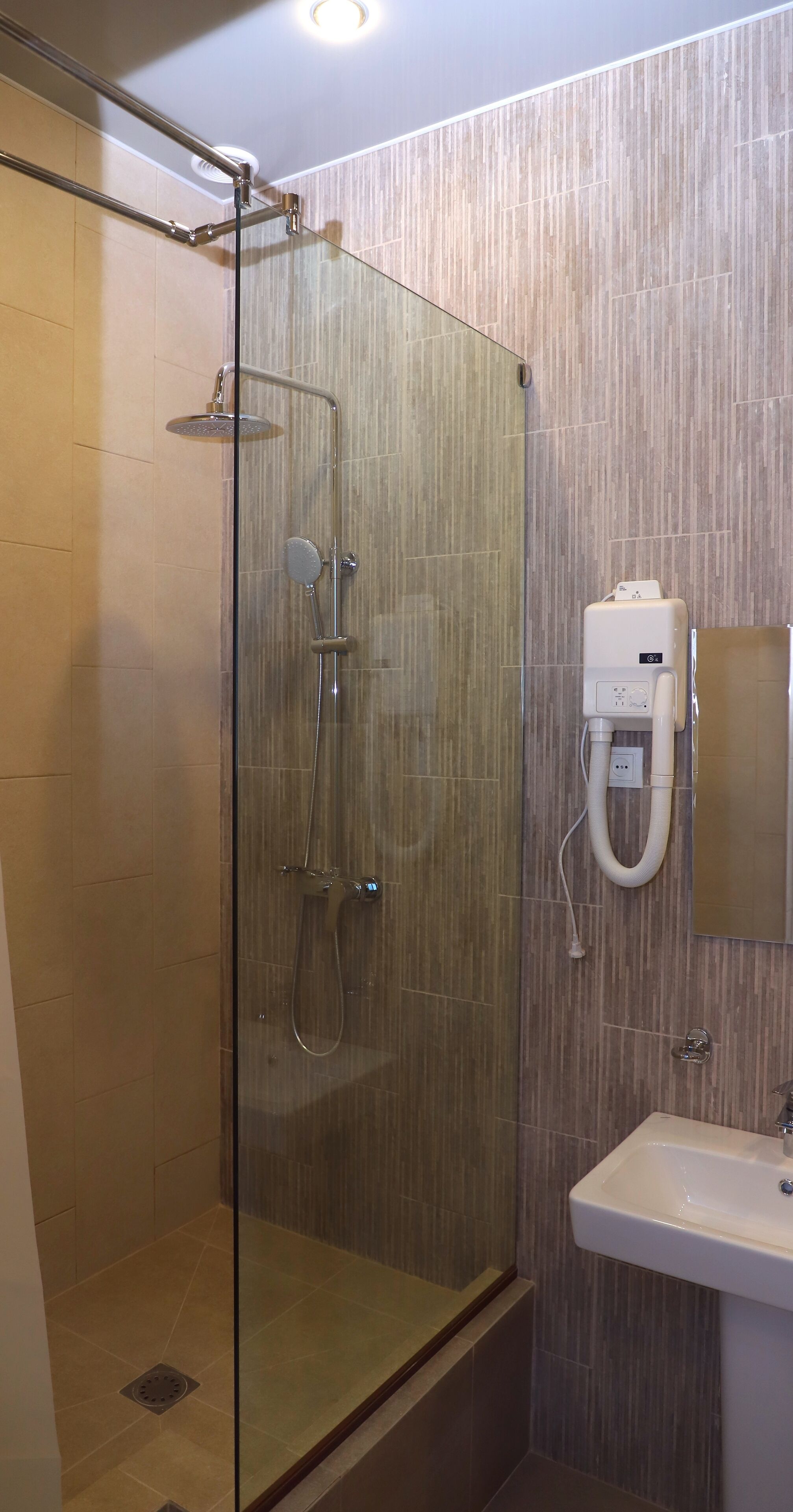 A modern bathroom with a glass-enclosed shower, a wall-mounted sink, and a towel dispenser.