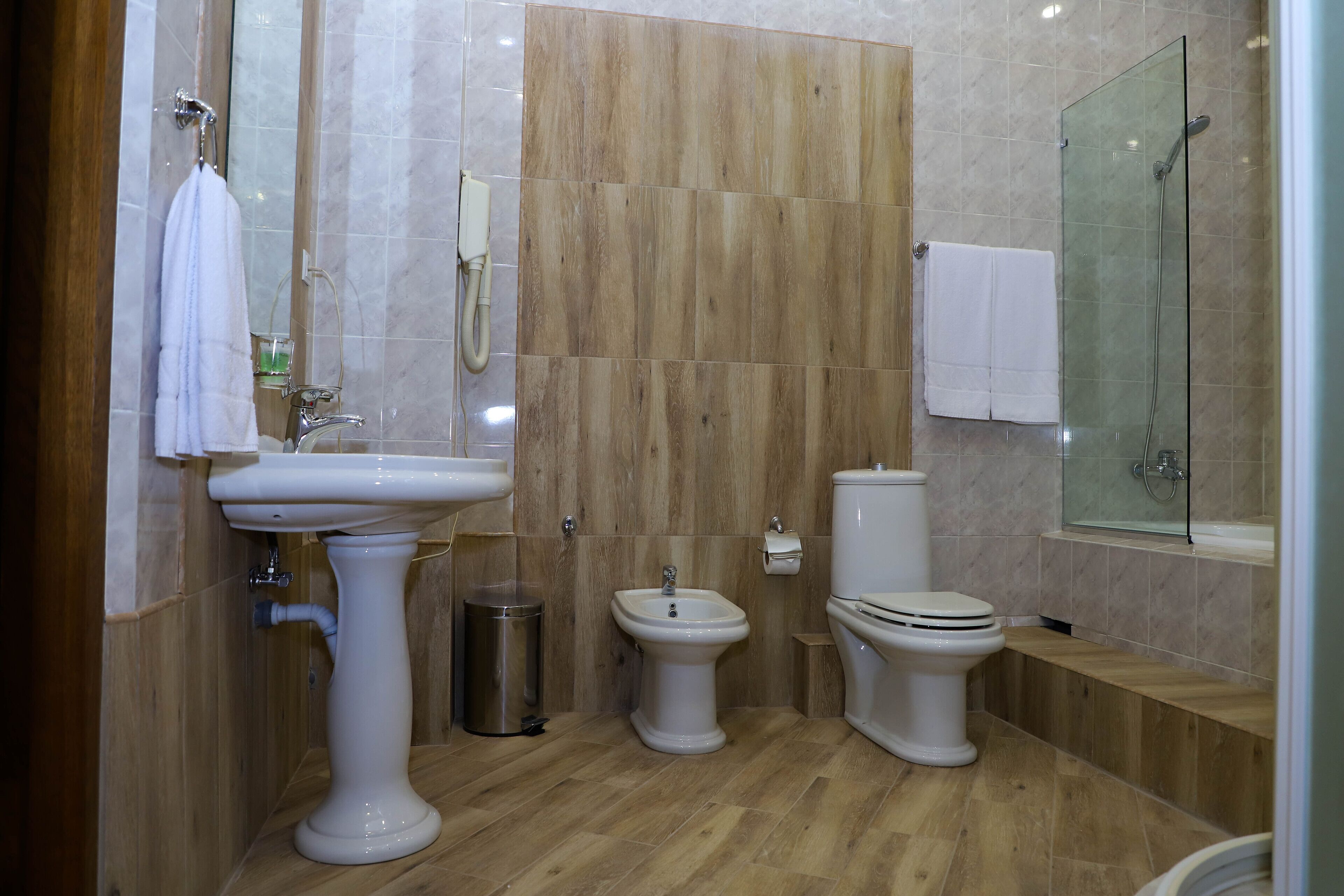 A modern bathroom with a pedestal sink, two toilets, a bidet, and a glass-enclosed shower.