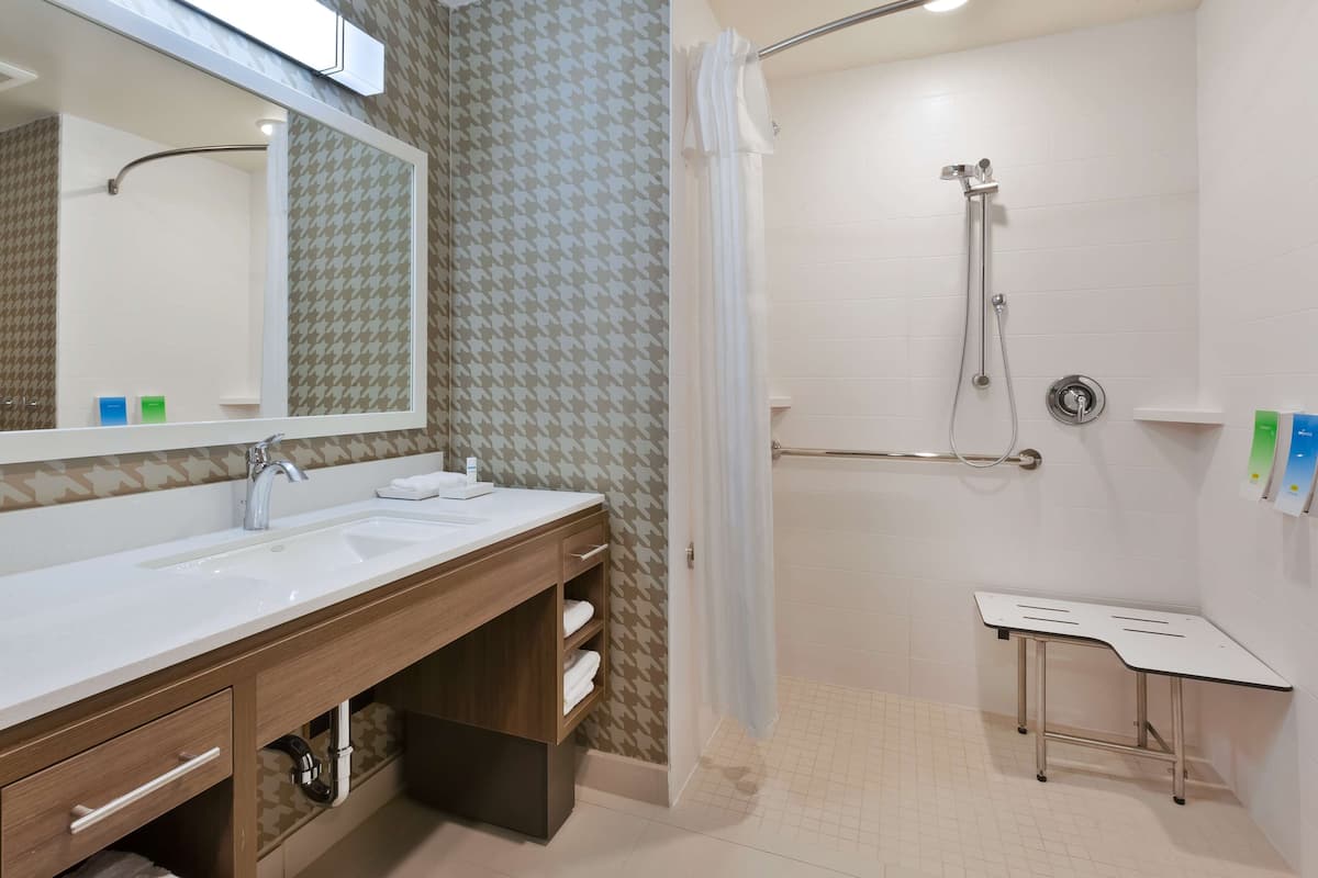 Ein Badezimmer mit einem großen Spiegel, zwei Waschbecken, einer Dusche mit Glastür und einem kleinen Tisch.