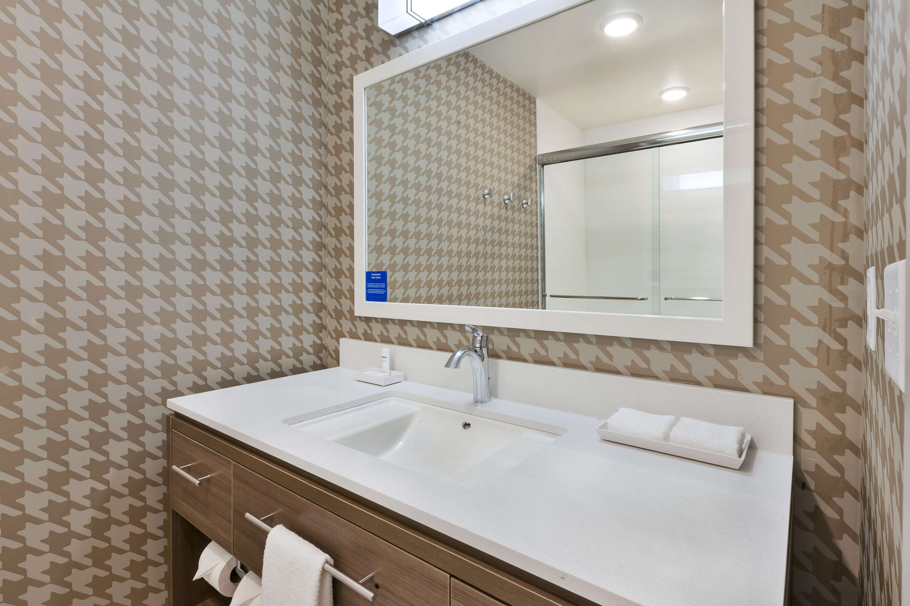 A bathroom with a white sink, a mirror, and patterned wallpaper.