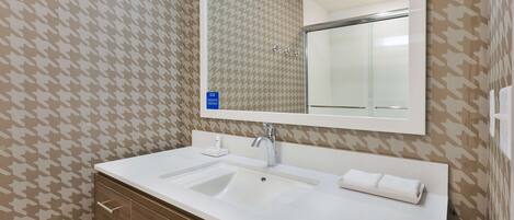 A bathroom with a white sink, a mirror, and patterned wallpaper.