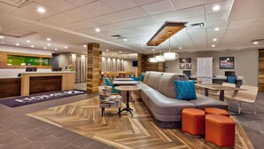 A modern hotel lobby with a reception desk, seating area, and a large window. - Home2 Suites by Hilton Battle Creek (Battle Creek)