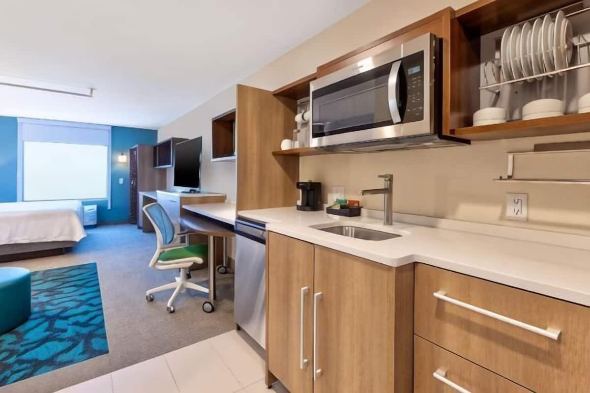 Ein kompaktes Hotelzimmer mit Küchenzeile, einem Bett, einem Schreibtisch und einem Fernseher.
