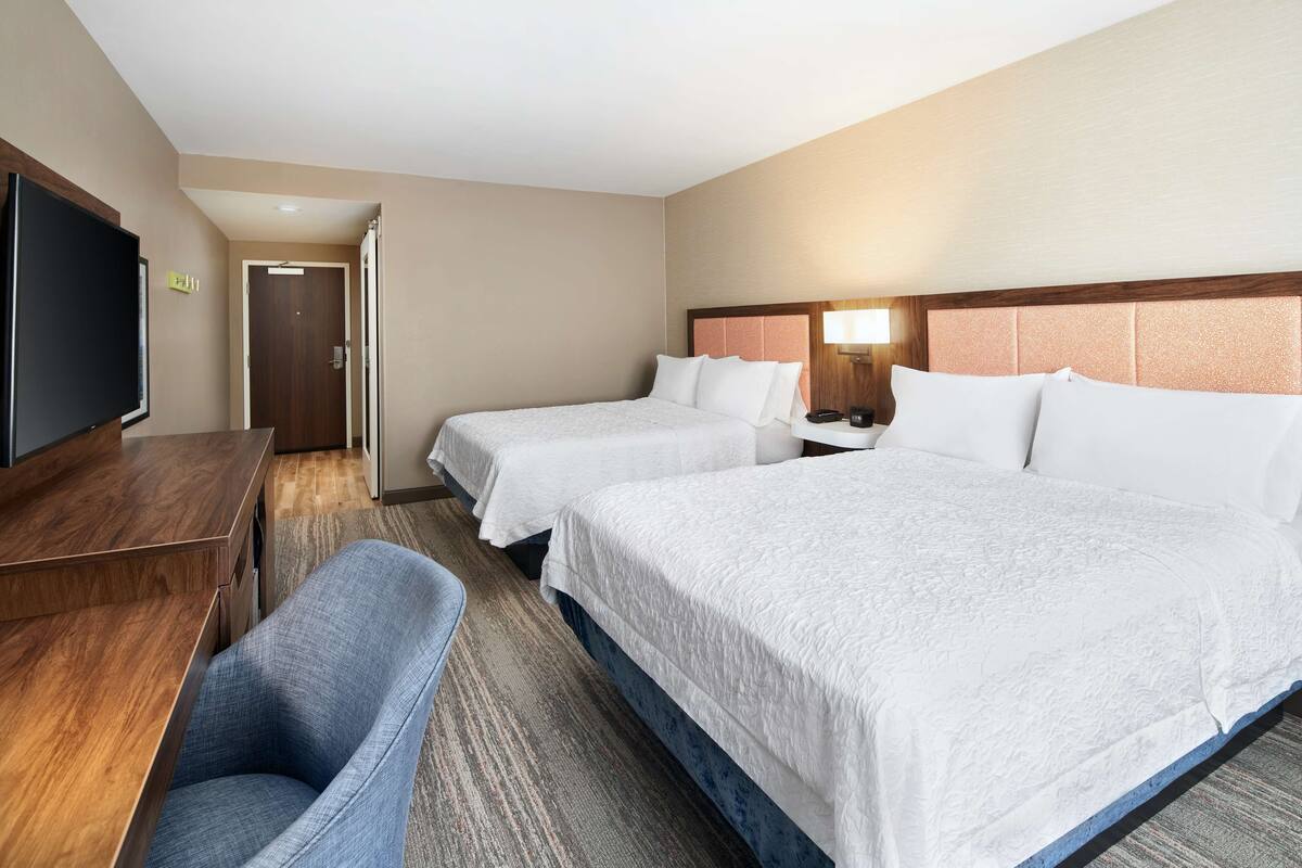 Ein Hotelzimmer mit zwei Betten, einem Schreibtisch, einem Fernseher und einem Sessel.