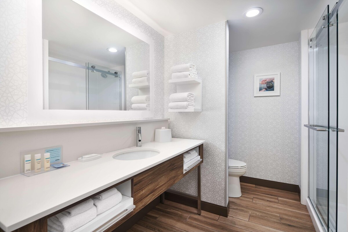 A modern bathroom with a large mirror, two sinks, a toilet, and a glass shower enclosure.